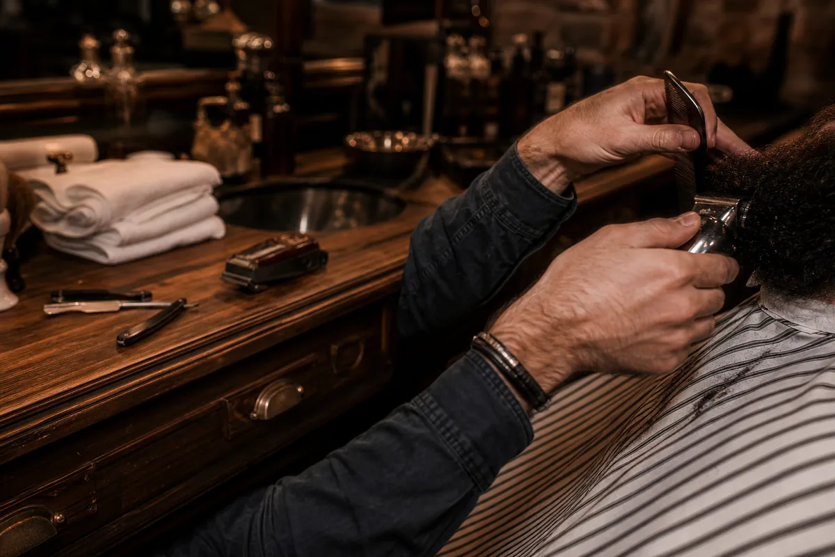 Fauteuil de barbier avec rasoir et tondeuse, un barbier taille une barbe dans une lumière chaude, mains cadrées sans visage